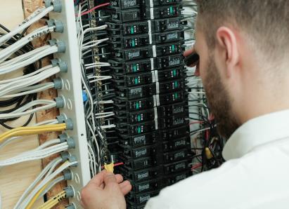 Francis electrical technician examining wiring connections inside a circuit breaker panel for a residential service check.