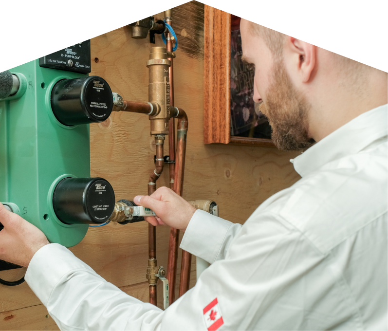 Francis HVAC specialist performing boiler installation, securing a valve on a new hydronic heating system with copper piping and a green circulation pump mounted on a wooden wall.