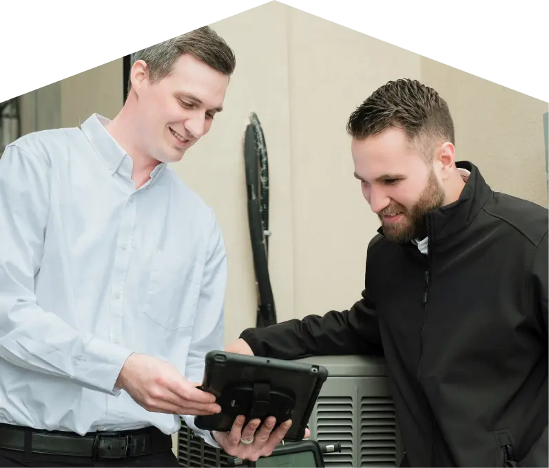 AC-Installation-banner-webp A Francis technician in a white shirt shows service details on a tablet to a smiling client in a black jacket, standing beside an AC unit outside a beige building.